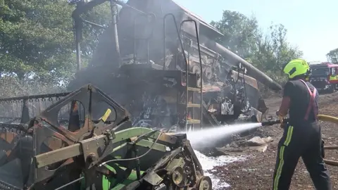 BBC Burnt farm machinery and firefighter with hose