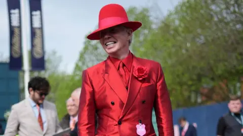 PA Media Racegoer dressed in red suit and matching hat at Aintree Ladies Day 2024