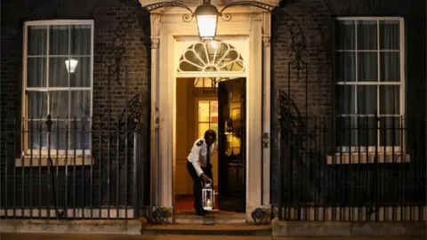 Reuters A doorman places a candle on the doorstep of Downing Street