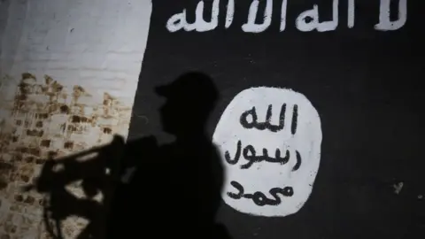 Getty Images A member of the Iraqi forces walks past a mural bearing the logo of the Islamic State (IS) group in a tunnel that was reportedly used as a training centre by the jihadists, on March 1, 2017, in the village of Albu Sayf, on the southern outskirts of Mosul