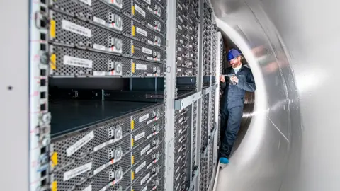 Microsoft A man in the tight confines of the opened tube works on a computer in a rack of identically sized machines