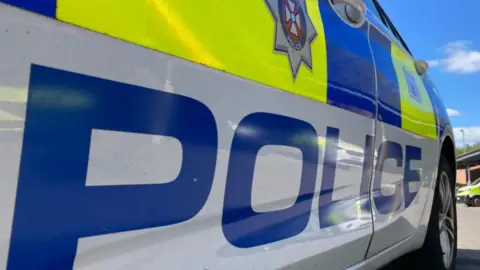 A close-up of the side of a white police car with blue and fluorescent yellow branding and with the word 'police' written across the doors in big bold blue letters.
