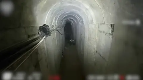 IDF A still taken from footage of an underground tunnel structure. Wires can be seen running along the concrete slab walls, with items of clothing in the background.
