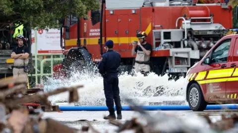 EPA A firefighter stands in front of a water hose with a fire extinguisher in the background, in the Valencia region of Spain.