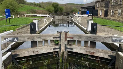 Two sets of lock gates with water dripping from the first ones and cascading down green moss.