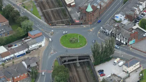 Network Rail An aerial view of a bridge running underneath a large roundabout which has four roads coming out of it. 