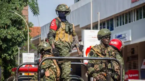 EPA Members of Ugandan security forces stand guard outside the Uganda Parliament during an anti-corruption march in Kampala, Uganda, 23 July 2024. Four men in soldiers uniforms are seen stood on the back of a truck.