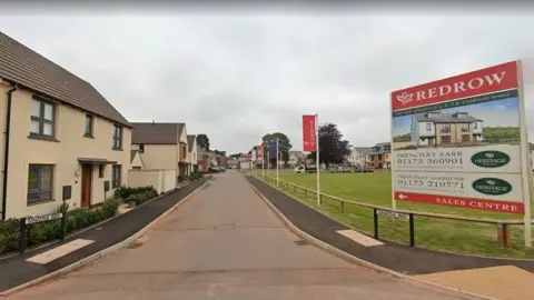 Google The image depicts a housing estate in Frenchay, Sinatra Way. Houses line the left of the image, while there's a green space to the right. In the right foreground there's a real estate sign advertising houses, with the name Redrow written on the top. 