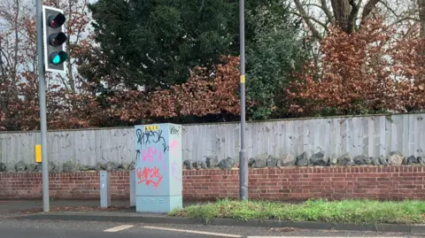 LDRS A street with a set of traffic lights and a telegraph pole. An electrical cabinet on the side of the road has been graffitied.