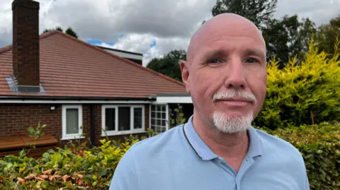 Man in a light blue polo shirt looks at the camera 