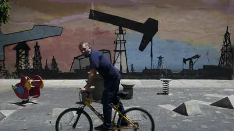 A person on a bike rides past graffiti depicting an oil drilling operation in Caracas in 2020.