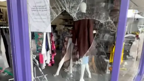 @bankonDave Screengrab of a window with a huge gap with shatter marks all around. Behind it are mannequins and clothes on sale in the shop.