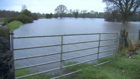 A rural field is seen flooded with rain water. There is a fence in the forefront of the image. 
