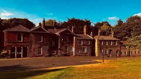 Andy Kershaw A grand red brick mansion on a sunny day surrounded by trees and green space