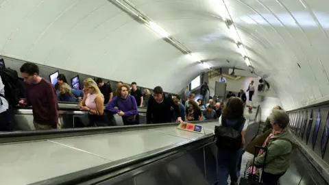 People standing on escalators as they travel up and down from the Tube platforms. 