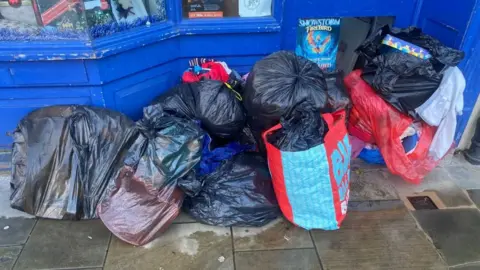 Handout A pile of full black bin bags sit outside a shop door.