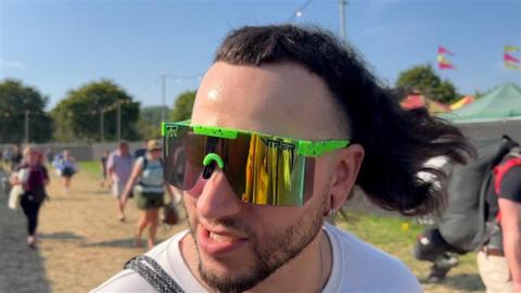 Image of a man with a mullet. He is wearing green reflective sunglasses. 