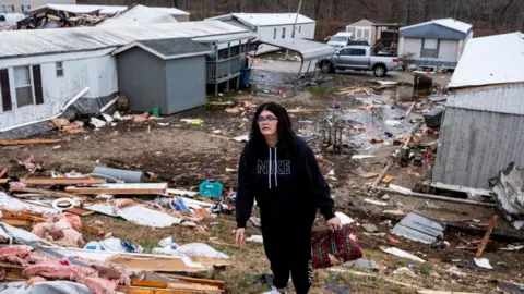 A woman wearing dark clothing stands amidst rubble