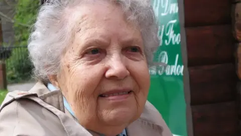 A picture of Frances Norris, an elderly woman with white hair and a stone-coloured coat. 