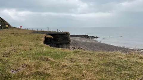 Part of a fence dangling from the cliff edge.