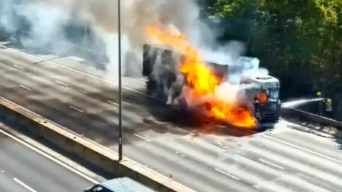 A lorry with a white cab on fire on a motorway