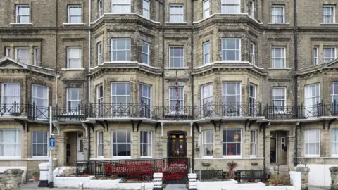 Kitchener's Guest House Kitchener's Guest House, a five storey Victorian mid-terraced house with bow windows on either side of the front door and extending up over four storeys. It is built from a yellowish brick and has a wrought iron black balcony across its first floor. Many red poppies are attached to the fence in front of its left hand ground floor window.