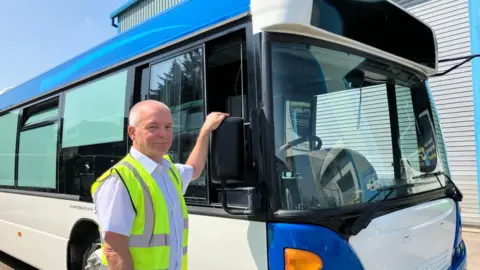 Bill Hiron in a high-visibility vest with his hand on the wing mirror of his bus