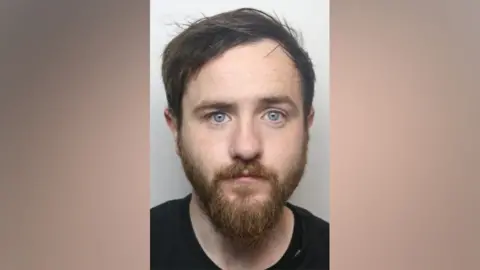 West Yorkshire Police Police custody image of Shea Conley. He is a white man with dark hear and a beard.