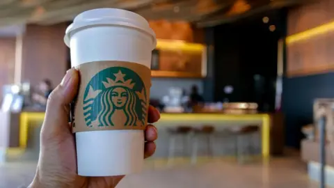 Getty Images Hand holding a coffee cup in a Starbucks coffee shop