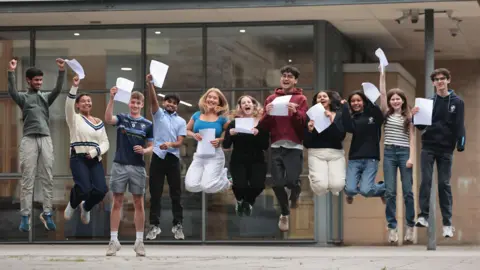 Students receiving their A-level results at Rathmore Grammar School in Finaghy, Belfast - 11 of them, a mix of boys and girls, all happily jumping in the air outside the school with their paper results in hand