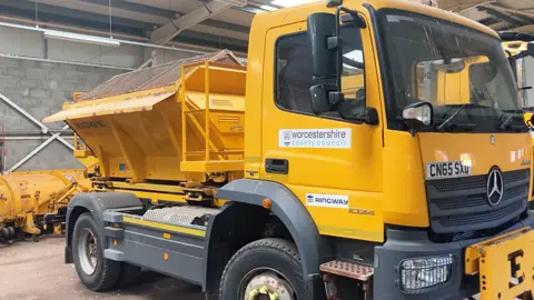 A yellow gritting lorry at a depot