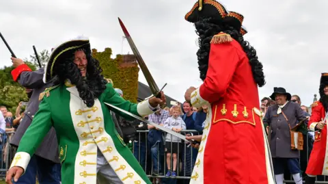 King William's actor wearing a red military coat pretends to stab King James, wearing a green coat, with a sword signalling the victory