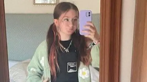Family handout Lucy Curtis is wearing a cardigan with flowers on it and is posing in the mirror taking a selfie, wearing glasses.
