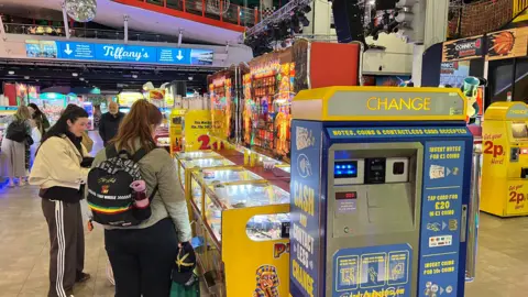 The inside of the pier showing various penny drop machines and a large blue machine for giving change. Several people are near the machines.