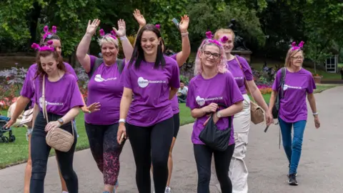 Kidney Research UK Seven people wearing purple Kidney Research UK t-shirts walking along a path. Two are holding up their arms.