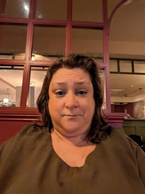 Amy Miles Amy is wearing a brown green top and has shoulder length brown/auburn hair.