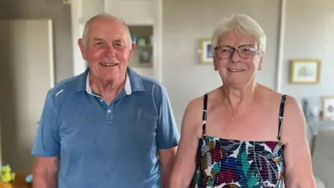 A man and a woman stand side by side in a living room.