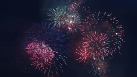 Getty Images Fireworks exploding in the night sky, they are mostly red but there are also blue and green bursts of light