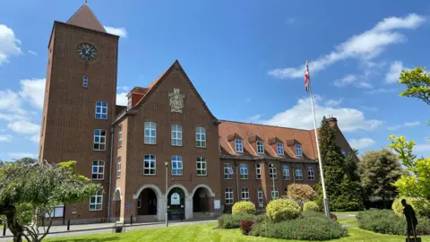 A large brick building with an area of green grass in front of it and blue sky above it. 