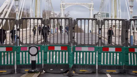 Green barriers can be seen across the road, blocking the entrance to the bridge
