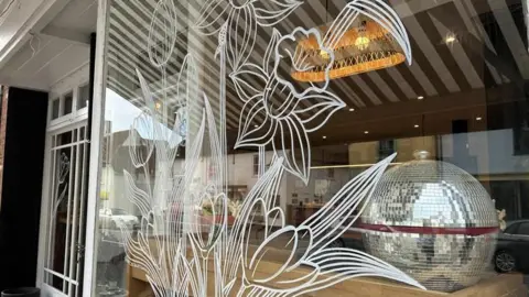 Jenny Kirk/BBC A painted white, floral mural can be seen on the frontage of a shop window.