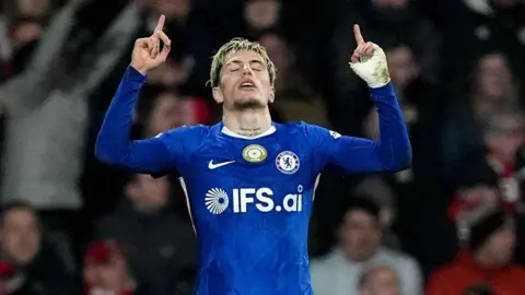 PA Media Garnacho in his blue Chelsea strip celebrates on his knees with his fingers pointing upwards after scoring a goal against Wrexham in the FA Cup.