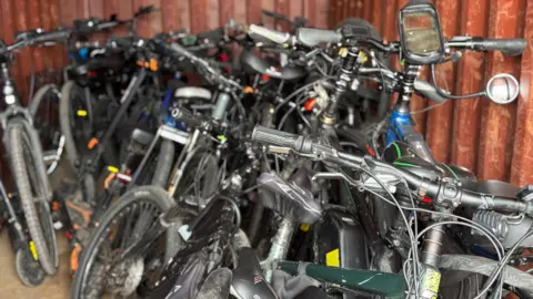 BBC A large pile of mountain bikes stacked up next to each other inside an orange metal shipping container.