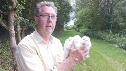 Man holding three young owls in a green space