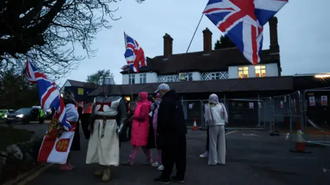 Reuters Protesters gather outside the Bell Hotel in Epping, holding Union Jacks and wearing knight costumes.