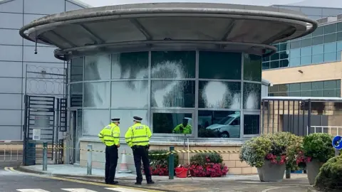 White paint on the side of a circular building. Two police officers in hi-viz uniforms are standing in front of the building.