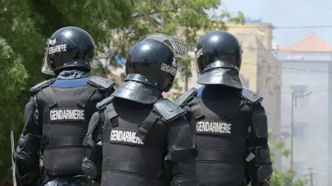 Senegalese gendarmes, in dark uniform and helmets, stand on a street corner in Dakar