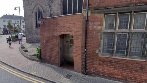 A small brick built public toilet block next to a church