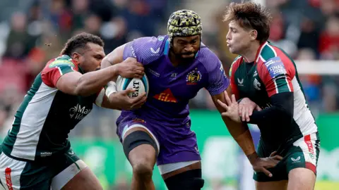 Exeter Chiefs' Christ Tshiunza bursts through the challenges of two Leicester Tigers players