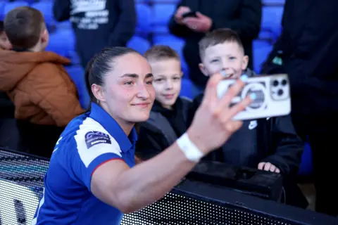 A player with blue kets with two young boys takes a selfie.